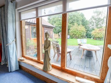 A large window with a statue on the wooden windowsill and outdoor wooden chairs and table at The Lodge in Hickling near Catfield