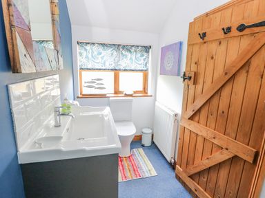 A bathroom with a sink, toilet, wooden door, radiator, window with patterned blind and fish decor at The Lodge in Hickling near Catfield