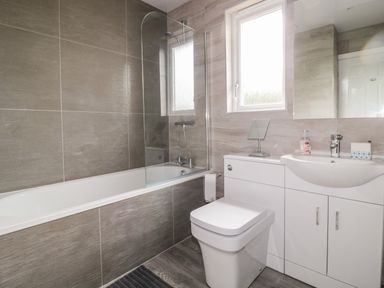 A bathroom with a bathtub shower combination toilet and sink with cabinet at Sea View Lodge in Eastfield Hall near Warkworth