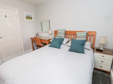 A bedroom with a wooden bed frame a desk with a chair bedside tables with lamps and a wall mirror at Sea View Lodge in Eastfield Hall near Warkworth
