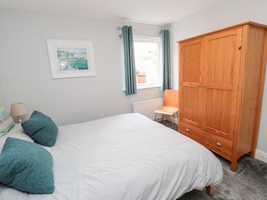 A bedroom with bed pillows a wooden wardrobe a wooden chair and a window with curtains at Sea View Lodge Eastfield Hall near Warkworth