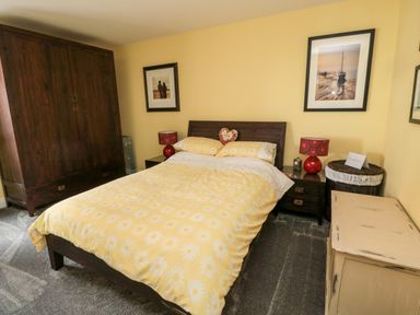 A bedroom with a double bed with yellow floral bedding dark wooden furniture and framed pictures on yellow walls at Sea View Lodge Eastfield Hall near Warkworth
