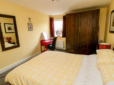 A bedroom with a yellow floral bedspread a red desk with a black chair a large wooden wardrobe and a window with red curtains at Sea View Lodge Eastfield Hall near Warkworth