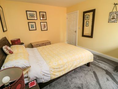 A bedroom with a bed with yellow flowered bedding a wooden headboard a bedside table with a lamp and framed pictures on yellow walls at Sea View Lodge in Eastfield Hall near Warkworth