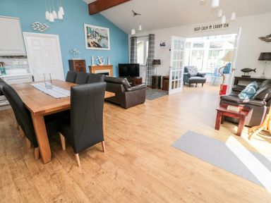 An open living and dining area with wooden floor black chairs leather sofas and a blue accent wall with nautical decor at Sea View Lodge in Eastfield Hall near Warkworth