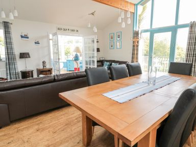 A dining area with a wooden table and leather chairs next to a sitting area with brown sofas and large windows at Sea View Lodge in Eastfield Hall near Warkworth