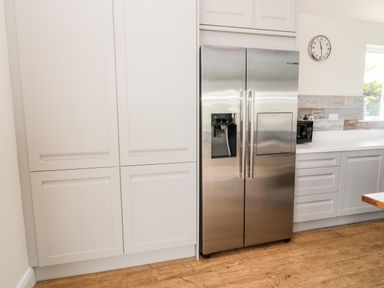 A kitchen with a stainless steel refrigerator white cabinets a microwave a wall clock and wooden flooring at Sea View Lodge Eastfield Hall near Warkworth