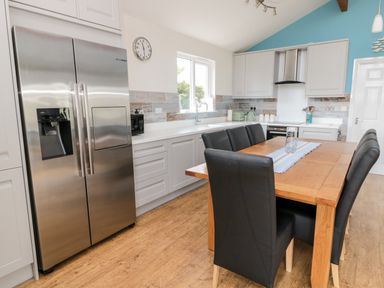 A kitchen with a wooden dining table and black chairs a stainless steel fridge and white cabinets at Sea View Lodge in Eastfield Hall near Warkworth