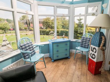 A sunroom with two blue chairs with fish patterned cushions a blue chest of drawers and a nautical-themed lamp at Sea View Lodge in Eastfield Hall near Warkworth