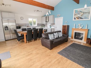 A kitchen and living area with a wooden dining table and black chairs brown leather sofa and a fireplace at Sea View Lodge Eastfield Hall near Warkworth