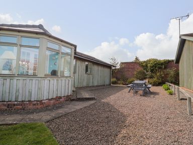 An outdoor area with gravel ground and wooden chairs and table near green wooden buildings at Sea View Lodge in Eastfield Hall near Warkworth