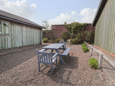 An outdoor seating area with picnic table and chairs between two wooden buildings at Sea View Lodge in Eastfield Hall near Warkworth
