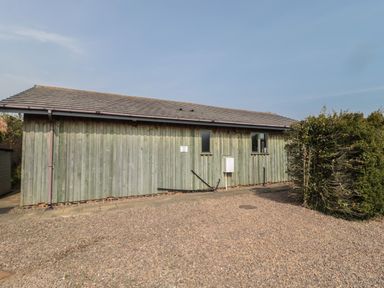 A single-story wooden building with two windows and a gravel driveway at Sea View Lodge in Eastfield Hall near Warkworth