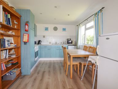 A kitchen and dining area with blue cabinets wooden dining table chairs and a bookshelf at Trevone - Chalet 130 in St Merryn near Padstow