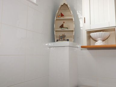 A corner of a room with white tiled walls and a boat-shaped shelf holding model boats at Trevone - Chalet 130 in St Merryn near Padstow