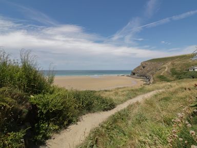 A coastal path with grass and bushes leading to a sandy beach and sea with cliffs and houses in the background at Trevone - Chalet 130 in St Merryn near Padstow