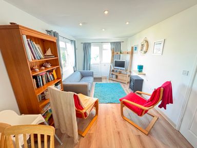 A living room with a bookshelf a sofa two chairs a rug and a TV at Trevone - Chalet 130 in St Merryn near Padstow