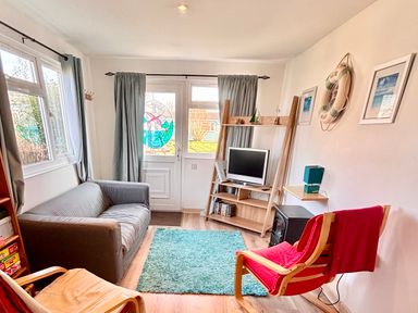 A living room with a grey sofa red chair wooden shelves and a small television at Trevone - Chalet 130 in St Merryn near Padstow