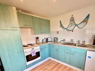 A kitchen with green cabinets a stove oven toaster kettle and sink with a drying rack at Trevone - Chalet 130 in St Merryn near Padstow