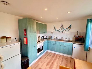A kitchen with blue cabinets a white refrigerator oven toaster kettle microwave and sink at Trevone - Chalet 130 in St Merryn near Padstow