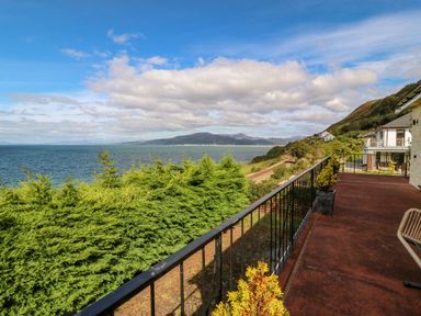A balcony with railings overlooking trees water and mountains at Machlud Haul in Llwyngwril