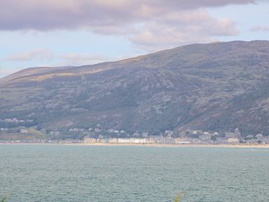 A coastal town with buildings along the shoreline and hills in the background at Machlud Haul in Llwyngwril