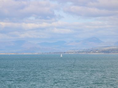 A large body of water with a sailboat in the distance and mountains and clouds in the background at Machlud Haul in Llwyngwril