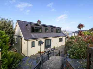 A two-story house with multiple windows and a basketball hoop by the entrance surrounded by greenery and a paved pathway at Machlud Haul in Llwyngwril