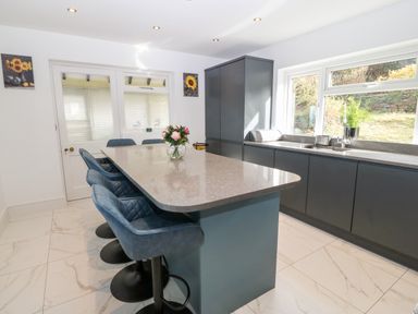 A kitchen with a countertop island and blue chairs at Machlud Haul in Llwyngwril