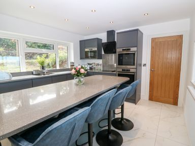 A kitchen with a large island countertop blue bar stools and modern appliances at Machlud Haul in Llwyngwril