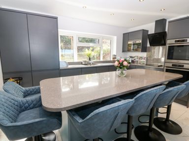 A kitchen with a large island, blue chairs, gray cabinets, and a window at Machlud Haul in Llwyngwril