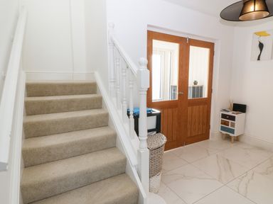 A staircase with carpeted steps next to wooden double doors and a small cabinet on a tiled floor at Machlud Haul in Llwyngwril