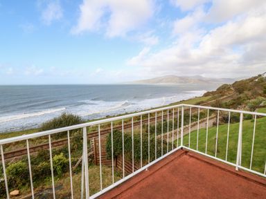 A balcony with white railing overlooking railway tracks and the sea with hills in the background at Machlud Haul in Llwyngwril