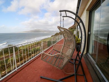 A balcony with a hanging wicker chair overlooking the sea and mountains at Machlud Haul in Llwyngwril