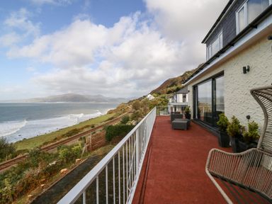 A balcony with outdoor furniture and potted plants overlooking railway tracks and the sea at Machlud Haul in Llwyngwril