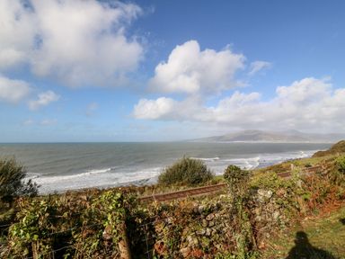 A coastal landscape with railway tracks and hills in the background at Machlud Haul in Llwyngwril