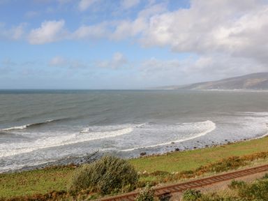 A coastal view with waves washing onto a rocky shore with railway tracks in the foreground at Machlud Haul in Llwyngwril