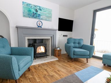 A living room with two blue armchairs a fireplace with a wood-burning stove and a wall-mounted television at Machlud Haul in Llwyngwril