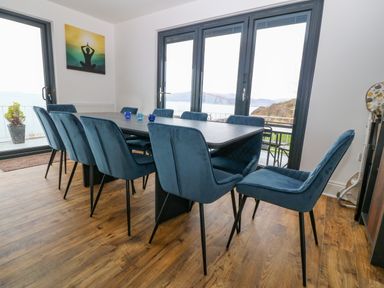 A dining room with a large table surrounded by blue chairs and glass doors overlooking a sea view at Machlud Haul in Llwyngwril