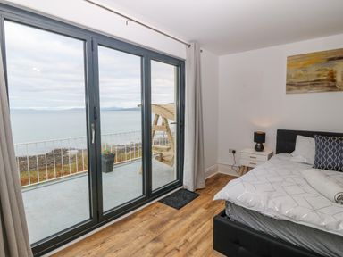 A bedroom with a bed a nightstand and a lamp overlooking a balcony with a sea view at Machlud Haul in Llwyngwril