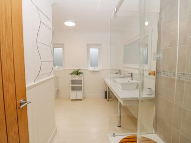 A bathroom with double sinks a glass shower enclosure a small cabinet with a plant and two frosted windows at Machlud Haul in Llwyngwril