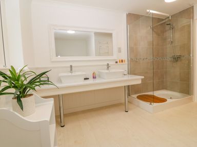 A bathroom with two white sinks under a large mirror and a glass shower enclosure with beige tiles and a wooden mat at Machlud Haul in Llwyngwril