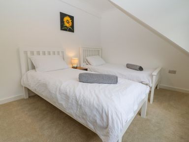 A bedroom with two single beds white bedding bedside table lamp and sunflower painting on wall at Machlud Haul in Llwyngwril