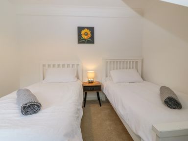 A bedroom with two single beds a nightstand with a lamp and a sunflower picture on the wall at Machlud Haul in Llwyngwril