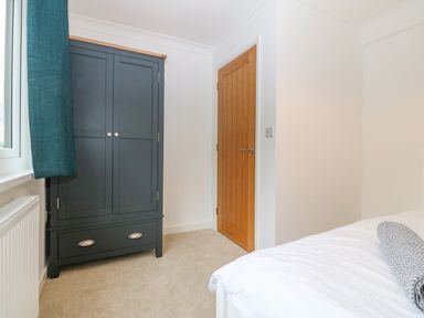 A bedroom with a black wardrobe a wooden door a bed with white bedding and a gray bolster pillow at Machlud Haul in Llwyngwril