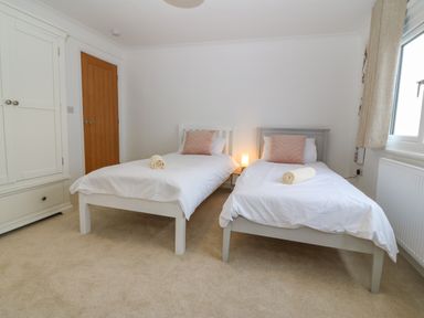 A bedroom with two single beds each with a pink pillow and rolled towel a nightstand with a lamp a white wardrobe and a wooden door at Machlud Haul in Llwyngwril