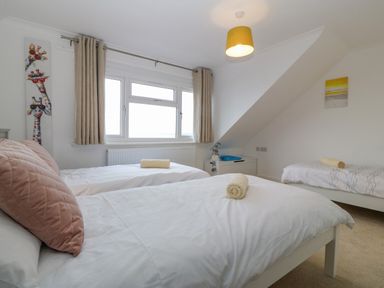 A bedroom with three single beds with white bedding each with a rolled towel a window with beige curtains and giraffe artwork on the wall at Machlud Haul in Llwyngwril