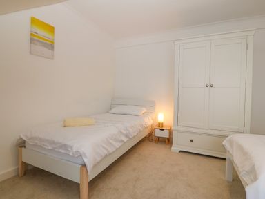 A bedroom with two single beds a nightstand with a lamp and a white wardrobe at Machlud Haul in Llwyngwril