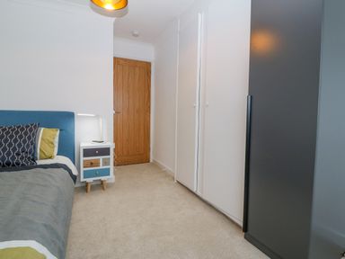 A bedroom with a bed a bedside table with a lamp white wardrobes and a wooden door at Machlud Haul in Llwyngwril