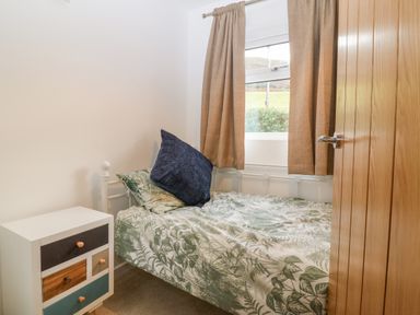 A small bedroom with a single bed covered with leafy patterned bedding and a blue pillow next to a multicolored drawer unit at Machlud Haul in Llwyngwril